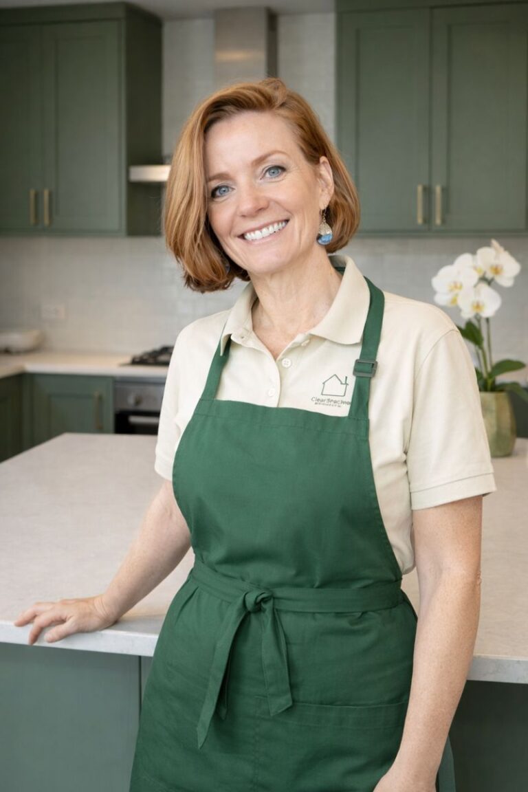 Debbie from ClearSpace Home smiling in an olive green apron in a minimalist kitchen